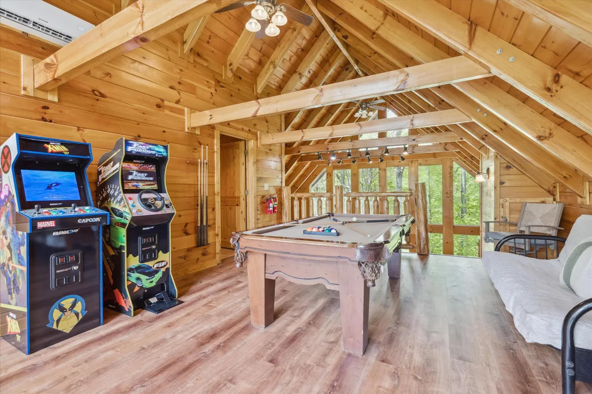 A vibrant game room featuring a pool table, classic arcade machines, and large windows with scenic views. The space is infused with natural light and designed for fun, group activities.