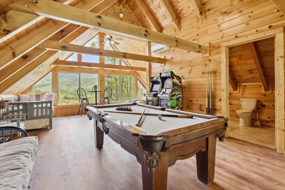 A vibrant, family-friendly game room with a pool table, arcade machine, large windows, and wooden beams. The setting is lively yet cozy, ideal for families to challenge each other to games and create lasting memories indoors.