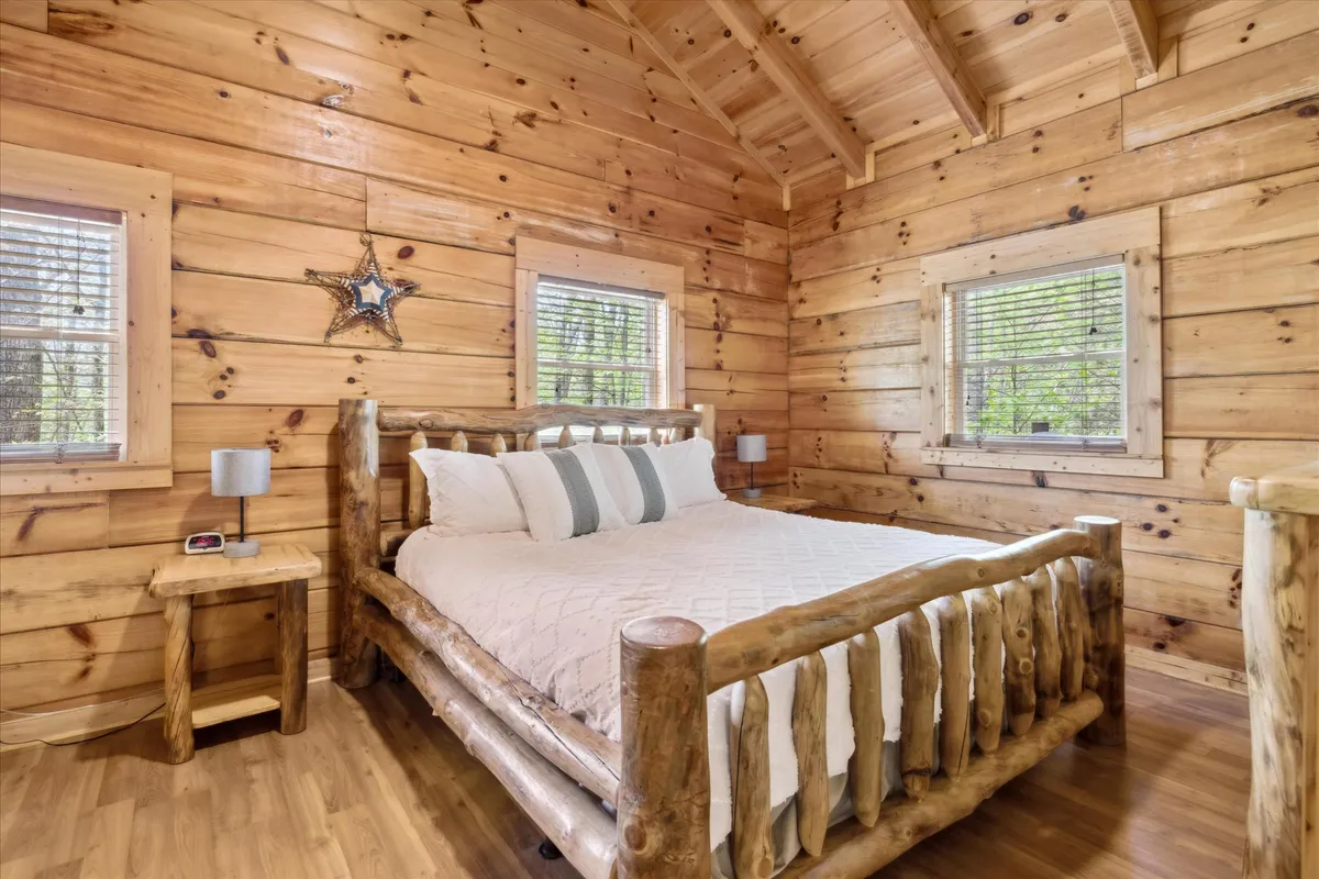 A peaceful bedroom featuring a rustic log bed, wooden side table, star decoration, and windows that let in gentle natural light. The serene ambiance is complemented by the view of nature outside, making this room a true sanctuary.