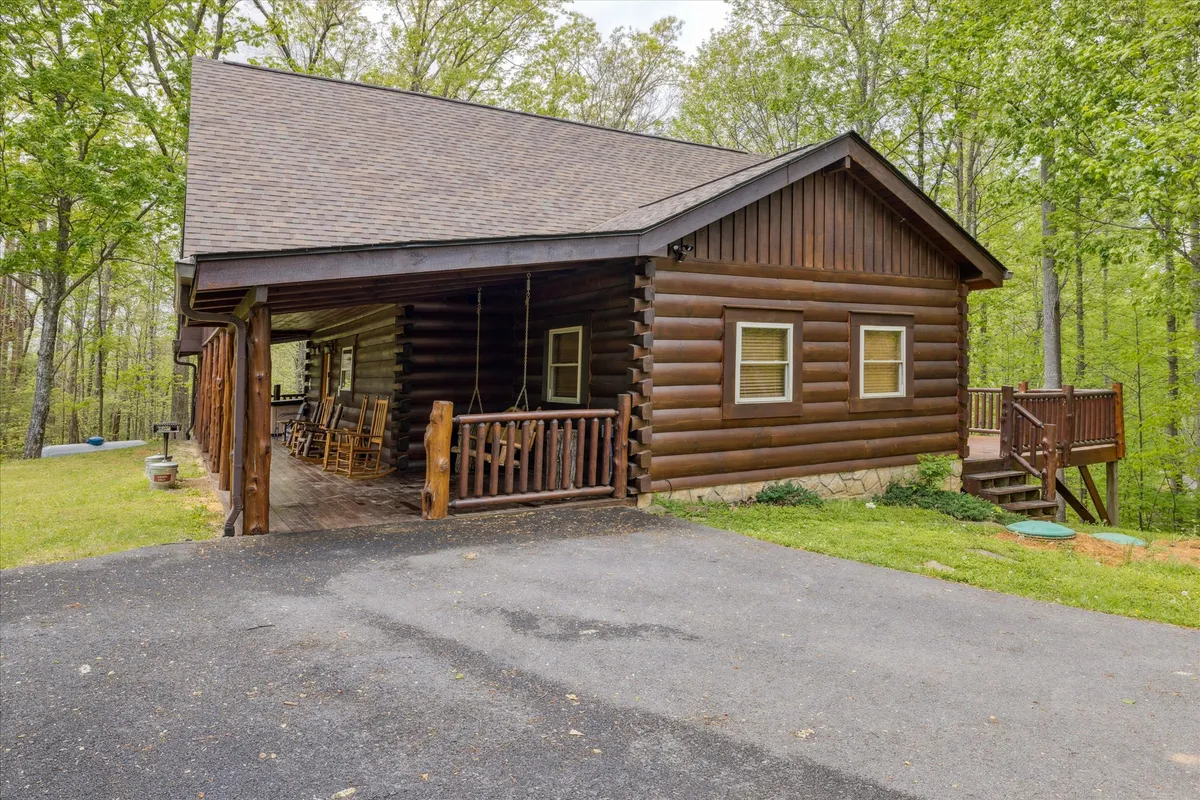 A cozy log cabin exterior with a welcoming porch featuring rocking chairs and lush greenery. The space suggests opportunities for outdoor relaxation, socializing, and enjoying the fresh mountain air as a family.