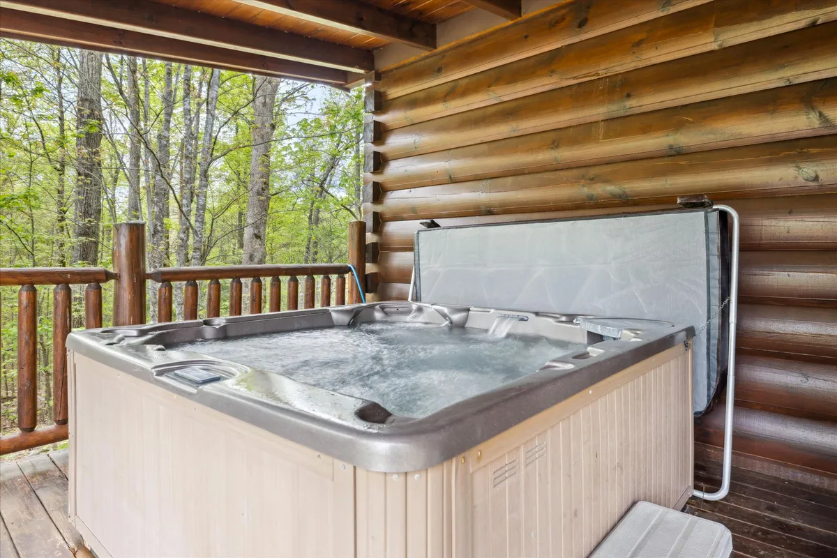 A tranquil wooden deck nestled among the trees, featuring a bubbling hot tub and ample space for guests to relax or socialize. The surrounding greenery provides privacy and a sense of connection to the Smoky Mountain landscape.