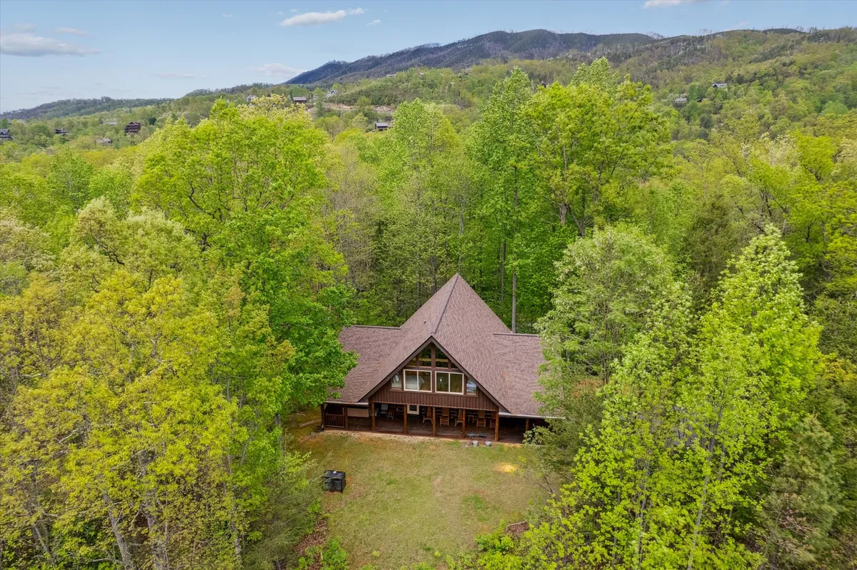 The hero image showcases the striking A-frame architecture of Looky Yonder Cabin, surrounded by lush greenery and framed by the majestic Smoky Mountains. The expansive porch offers panoramic sunset views, inviting guests to unwind amidst nature. The tranquil setting evokes feelings of peace, relaxation, and connection to the outdoors, with plenty of space for family gatherings or quiet moments with a morning coffee.