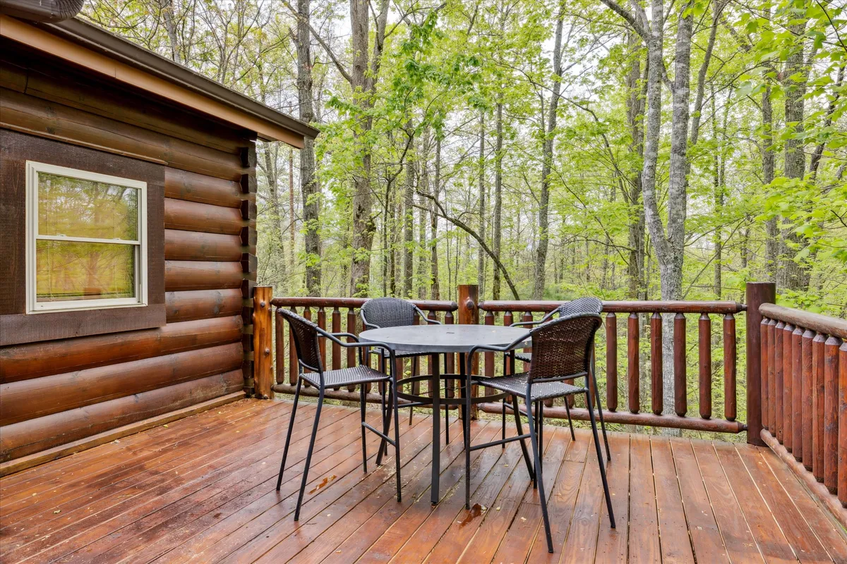 An inviting wooden deck featuring a round table surrounded by trees and connected to the cabin’s exterior. This peaceful spot is perfect for morning coffee, cozy afternoon reading, or romantic evening gatherings under the stars.