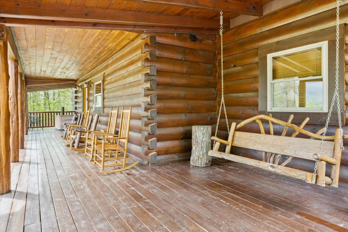 A cozy porch scene with rustic rocking chairs, a wooden swing, and solid log walls overlooking the serene outdoors. The setup hints at relaxation and opportunities to enjoy the mountain air after a day on the greens.