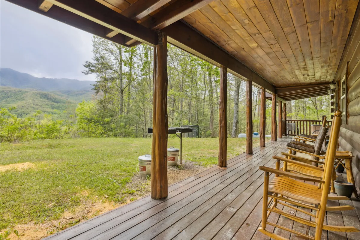 This image shows a wooden porch equipped with classic rocking chairs and a grill area, all overlooking a stunning mountain view. The porch is adorned with wooden flooring and surrounded by lush trees, capturing the sense of peaceful seclusion and natural beauty.