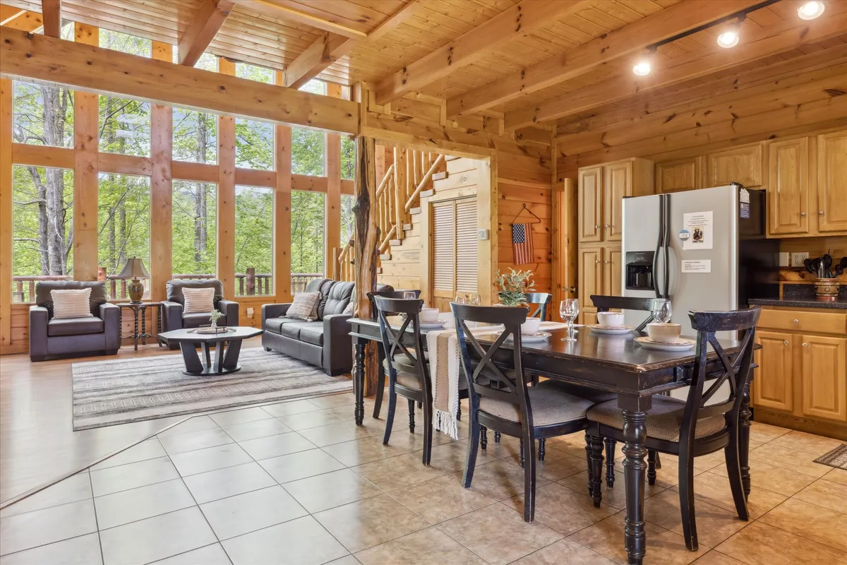 An open-plan space showcasing large windows, a dining table set for gatherings, a comfortable sofa, and a staircase. The layout emphasizes connectivity and the abundance of natural light.