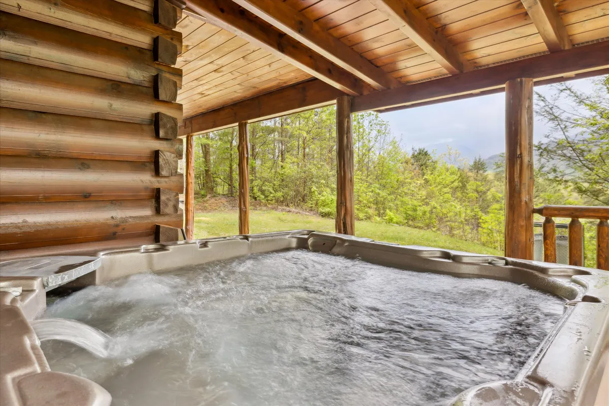 A cozy, sunlit corner featuring a private hot tub set against wooden beams and large windows. The space is infused with natural light, creating an inviting atmosphere for unwinding together while enjoying views of the surrounding trees and sky.